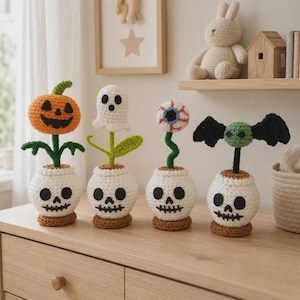 Peut inclure: Quatre décorations d'Halloween au crochet dans des pots blancs en forme de crâne. Les figurines comprennent une citrouille orange, un fantôme blanc, un globe oculaire rouge et blanc, et une chauve-souris verte aux ailes noires sur des tiges.