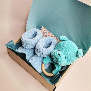 Peut inclure: Un ensemble cadeau pour bébé en crochet bleu dans une boîte brune avec un papier de soie bleu. L'ensemble comprend une paire de chaussons, un ours en crochet et un anneau de dentition en bois.