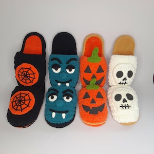 May include: A collection of Halloween-themed slippers. The slippers feature designs of a spider web, a vampire, a jack-o'-lantern, and a skull. The slippers are made of soft, textured material in black, orange, blue, and white.