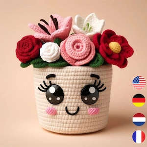 Puede incluir: Una maceta de flores de ganchillo con una cara sonriente, ojos grandes y pestañas. La maceta está llena de flores de ganchillo en tonos de rosa, rojo y blanco.