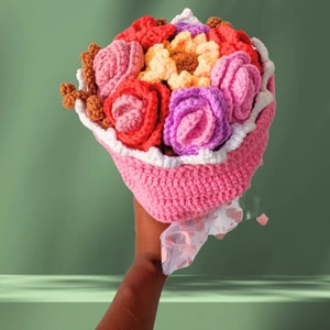 May include: A crocheted bouquet of flowers in shades of pink, red, purple, and yellow. The bouquet is wrapped in a pink crocheted paper with white trim.