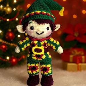 May include: A handmade crochet elf doll. The doll has a green hat and outfit, with yellow and red floral patterns. The elf has a smiling face, white ears, and brown boots. A Christmas tree and gifts are in the background.