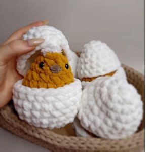Peut inclure: Trois poussins en crochet dans des coquilles d'œufs blanches. Le poussin au premier plan sort de sa coquille d'œuf. Les poussins sont dans un panier en osier brun.
