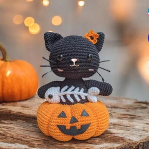 Peut inclure: Chat noir en crochet tenant un os en crochet blanc, assis sur un potiron en crochet orange avec un visage de citrouille.