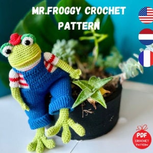 May include: Crochet pattern for a green frog wearing blue overalls and a red and white striped shirt. The pattern is available in English, Dutch, and French. The pattern is a PDF download.