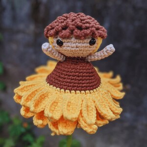 May include: A handmade crochet doll with a sunflower skirt and a brown mushroom cap. The doll has a tan face, arms, and a brown dress. The sunflower skirt is yellow and has detailed petals.