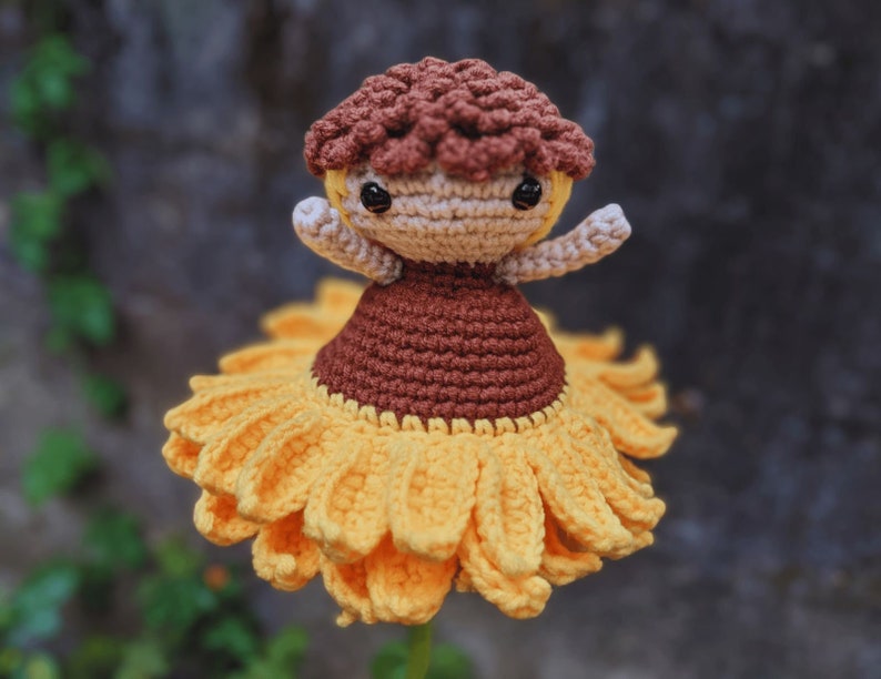 May include: A handmade crochet doll with a sunflower skirt and a brown mushroom cap. The doll has a tan face, arms, and a brown dress. The sunflower skirt is yellow and has detailed petals.