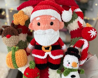May include: A handmade Christmas wreath featuring a crocheted Santa Claus, snowman, reindeer, star, and ornaments. The wreath has a red bow at the top and is decorated with red, white, green, and orange elements. A festive holiday decoration.