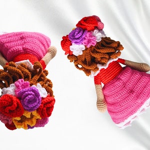 May include: Two crocheted dolls with brown hair and pink dresses. Each doll has a flower crown with red, pink, purple, white, and yellow flowers.