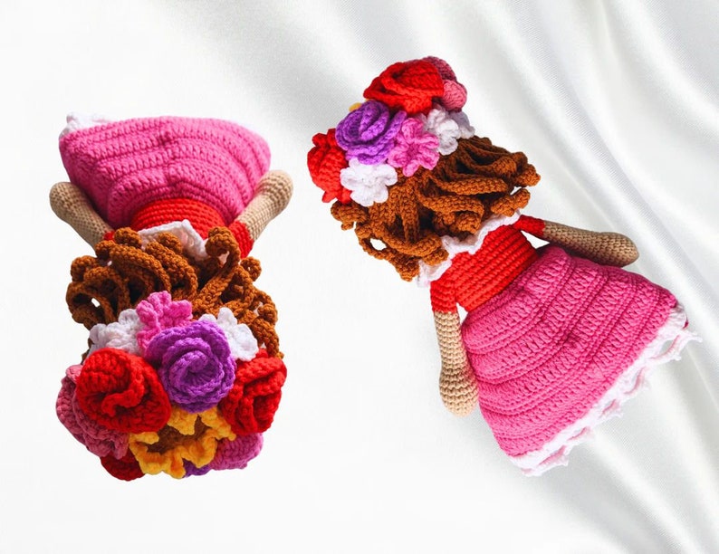 May include: Two crocheted dolls with brown hair and pink dresses. Each doll has a flower crown with red, pink, purple, white, and yellow flowers.