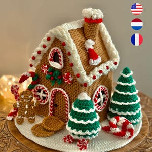 Op de afbeelding: Een gehaakt peperkoekhuisje met witte glazuurranden, rode kraalaccenten en een schoorsteen. Het huis heeft een deur, ramen en is versierd met een peperkoeken mannetje, zuurstokken en groene kerstbomen. Het huis staat op een houten voet.