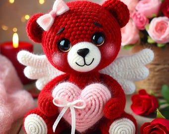 May include: A red crocheted teddy bear with white wings and a pink heart. The bear is wearing a pink bow and has a sweet expression.