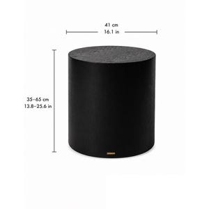 May include: A cylindrical black side table with a visible wood grain texture. The table has a diameter of 16.1 inches and an adjustable height ranging from 13.8 to 25.6 inches. A small rectangular gold-colored brand tag is attached at the base.