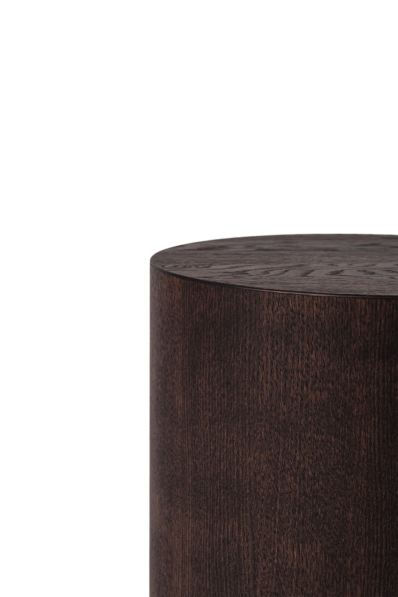 May include: A dark brown, cylindrical wooden side table. The table has a smooth, rounded top and a textured, vertical grain pattern. The wood has a rich, warm tone, and the design is simple and modern.