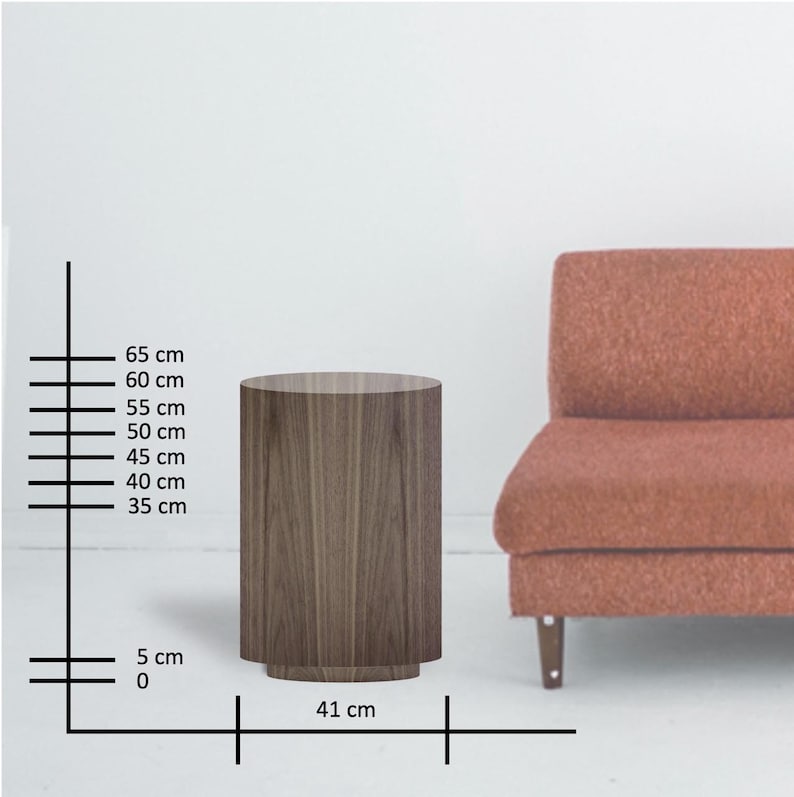 May include: A cylindrical wooden side table with a dark wood grain finish. The table is 25.6 inches tall and 16.1 inches in diameter. The table has a slightly wider base. A coral-colored sofa is in the background.