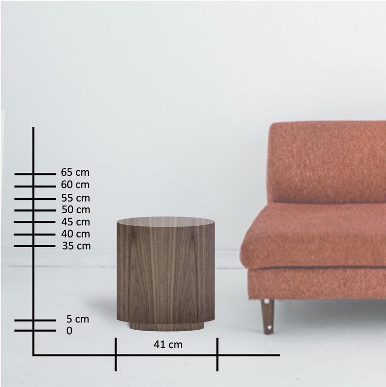 May include: A cylindrical wooden side table with a dark wood grain finish. The table is 16 inches in diameter and 26 inches tall. A reddish-orange sofa is partially visible in the background.