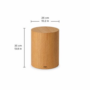May include: A cylindrical wooden stool with a light brown oak grain finish. The stool measures 26 cm in diameter and 35 cm in height. A small rectangular label is visible at the base of the side panel, indicating the product brand name.