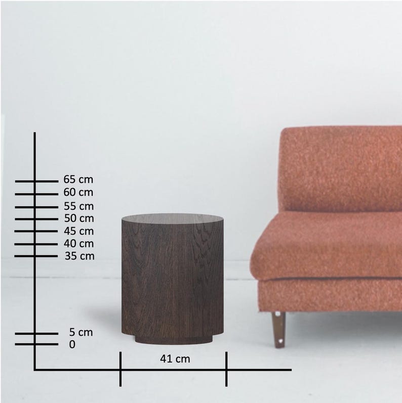 May include: A dark brown, cylindrical side table with a flat top and a slightly wider base. The table is approximately 16 inches wide and 26 inches tall. A rust-colored sofa is partially visible in the background.