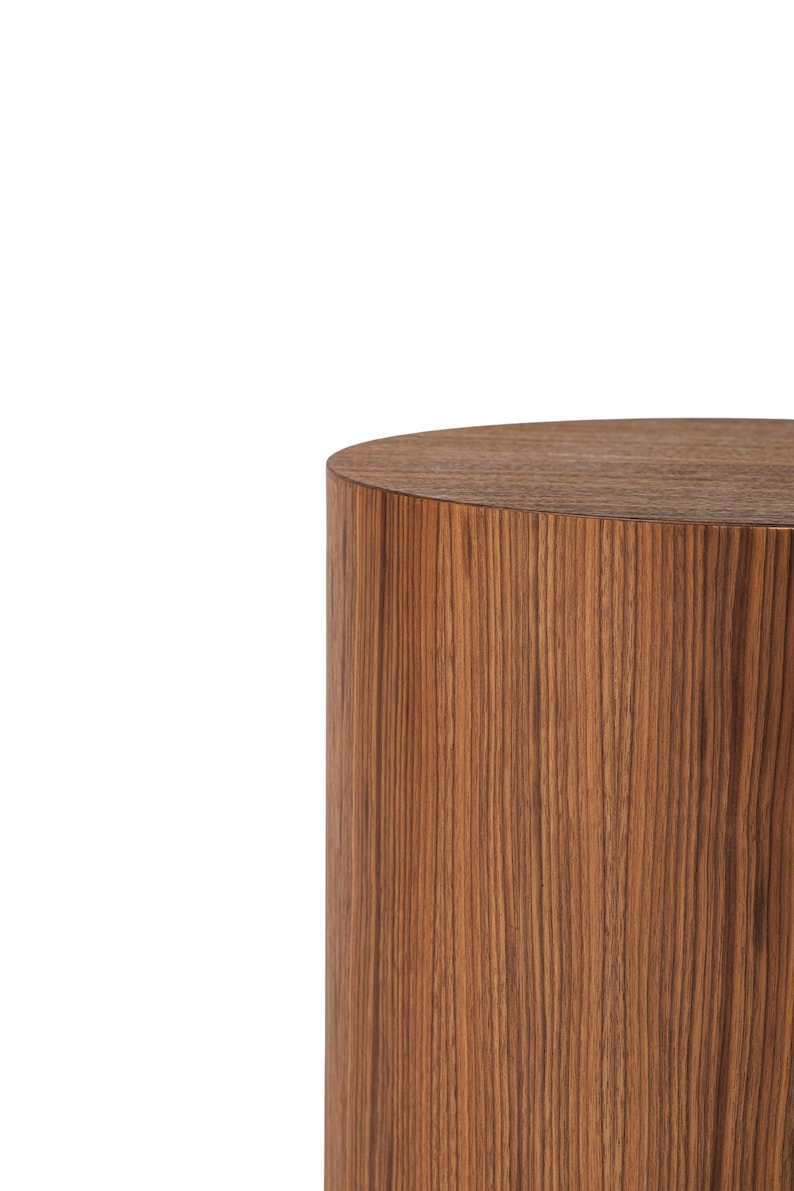 May include: A cylindrical wooden side table with a flat top. The table is made of a dark brown wood with vertical grain patterns. The design is simple and modern, suitable for various interior styles.