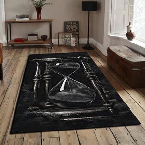 May include: A black and white area rug featuring a large hourglass design. The hourglass is the focal point, with detailed shading and a textured appearance. The rug has a dark, dramatic aesthetic, suitable for a living room or bedroom.