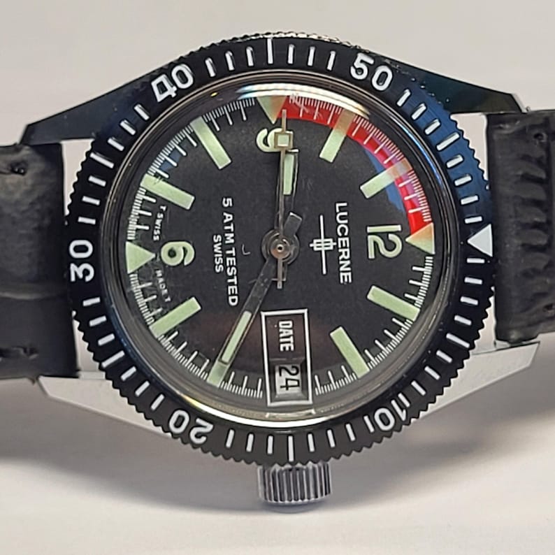 May include: A vintage Lucerne watch with a black dial, luminous hands and markers, and a date window at 3 o'clock. The watch has a black rotating bezel with white markings and a black leather strap. The watch is marked "5 ATM TESTED SWISS".