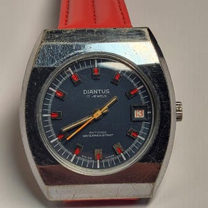 May include: A vintage silver-toned DIANTUS watch with a dark blue face, red accents, and a date display. The watch features a red leather strap. The watch face has the text "DIANTUS 17 JEWELS" and "ANTICHOC WATERRESISTANT".