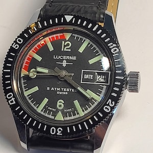 May include: A Lucerne watch with a black dial, luminous hands and markers, and a date display at the 3 o'clock position. The watch has a black rotating bezel and a black leather strap. The watch is marked "5 ATM TESTED SWISS".