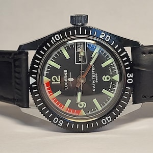 May include: A black Lucerne wristwatch with a black bezel and a black leather band. The watch face is black with white numerals and hands, and a red and white accent. The watch reads "5 ATM TESTED SWISS".