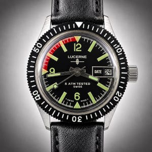May include: A black Lucerne watch with a black bezel and a black leather band. The watch face has luminous green markers and hands, with the text "LUCERNE" and "5 ATM TESTED SWISS". The date is displayed at the 3 o'clock position.