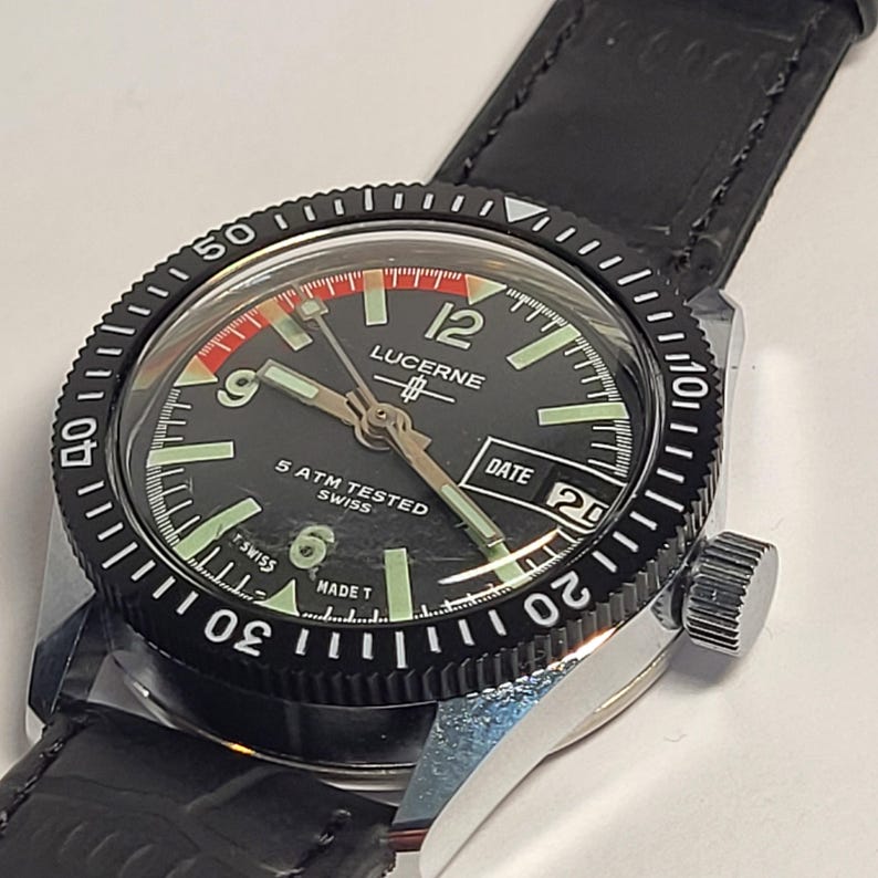 May include: A Lucerne Swiss watch with a black dial, luminous hands, and a date display. The watch has a black rotating bezel with white markings and a black leather strap. The watch face displays the text "LUCERNE" and "5 ATM TESTED SWISS".