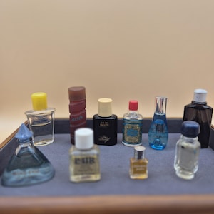 Pode incluir: Uma coleção de frascos de perfume em miniatura em uma caixa de madeira. Os frascos são de várias cores e formas, incluindo transparente, azul, vermelho e amarelo. Os frascos estão dispostos em um padrão de grade em uma superfície de feltro cinza.