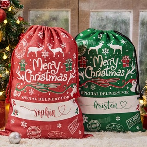 May include: Two red and green Christmas gift bags with a white "Merry Christmas" design and reindeer illustrations. The bags have a drawstring closure and are personalized with the names "Sophia" and "Kristen".
