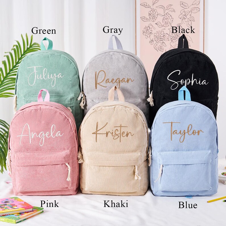 May include: A collection of corduroy backpacks in various colors: green, gray, black, pink, khaki, and blue. Each backpack features a name embroidered on the front. The backpacks have a front pocket and a top handle.