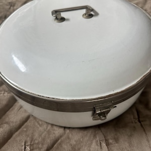 May include: White enamel round storage box with a silver metal lid and handle. The lid has a silver metal latch.