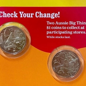 Puede incluir: Dos monedas australianas de 1 $ en soportes de plástico transparente. Las monedas presentan ilustraciones detalladas y se muestran sobre un fondo rojo y naranja con el texto "Check Your Change!" y "Two Aussie Big Things 2".