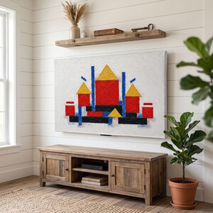 Puede incluir: Un cuadro rectangular sobre lienzo con fondo blanco texturizado y formas geométricas en rojo, amarillo, azul y negro. La obra está montada en una pared de listones blancos sobre un mueble de madera para televisión y un estante flotante.