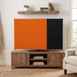 Puede incluir: Una funda rectangular para pantalla de televisión con un diseño bicolor que presenta una gran sección naranja a la izquierda y una sección negra más pequeña a la derecha, ambas con una superficie texturizada de estilo empaste al frente.