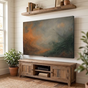 Könnte beinhalten: Ein rechteckiger, an der Wand montierter Fernseher, der ein abstraktes Gemälde mit vermischten Strichen in tiefem Waldgrün, gedämpftem Grau und leuchtendem Brandorange zeigt. Der Bildschirm befindet sich über einem rustikalen Holz-Medienboard.
