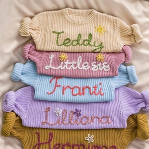 May include: A stack of five knitted jumpers with embroidered names, "Teddy", "Little Sis", "Franti", "Liliana", and "Hermione". Each jumper has a different colour and features embroidered flowers.