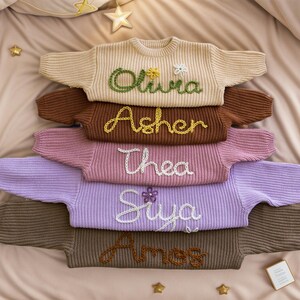 May include: A stack of six knitted sweaters in various colors, each with a different name embroidered on the front. The names are Olivia, Asher, Thea, Siya, and Ames.