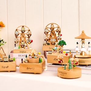 Pu&ograve; includere: Una collezione di carillon in legno con vari design. Alcuni presentano ruote panoramiche con personaggi animali, altri figure danzanti o trenini. Le scatole sono marrone chiaro e hanno nomi incisi.