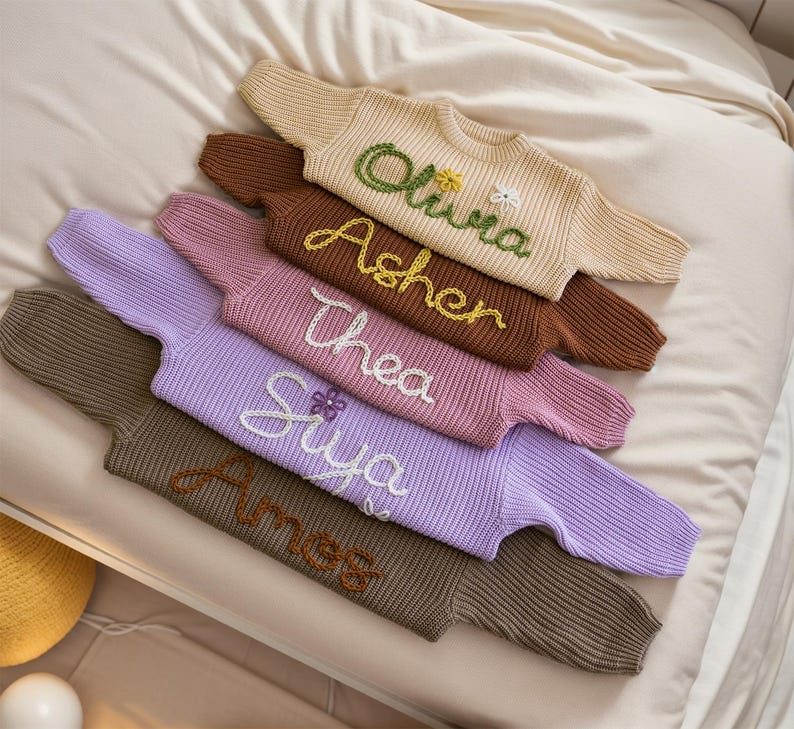 May include: A stack of five knitted jumpers in various colours, each with a different name embroidered on the front. The names are Olivia, Asher, Thea, Siya, and Amess.