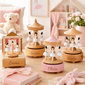 May include: Four wooden music boxes featuring miniature ballerinas in white and pink tutus. Two carousel-style boxes are engraved with the names Sophia and Amelia, one with Olivia, and a stage-style box is engraved with the name Emma.