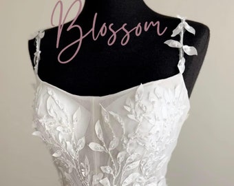 May include: A white tulle wedding dress with delicate floral embroidery and a fitted bodice. The dress has a flowing skirt and a simple, elegant design.
