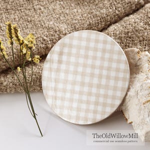 May include: A round, beige and white gingham pattern plate. The plate is set on a white surface with a beige textured fabric in the background. Dried yellow flowers and a piece of stone are also in the image. The text "TheOldWillowMill" is at the bottom.