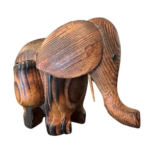 May include: A wooden elephant figurine with a detailed carved design. The elephant is brown with darker brown and black accents. The ears are large and the trunk is extended. The figurine is a decorative item.