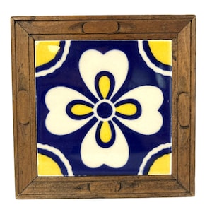 Könnte beinhalten: Eine quadratische Keramikfliese mit einem blauen, weißen und gelben Blumendesign ist in einem dunklen Holzrahmen gerahmt.