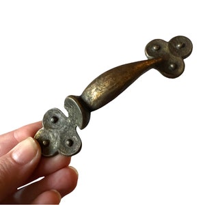 May include: A brass cabinet pull with a curved handle and a decorative clover-shaped design on each end.