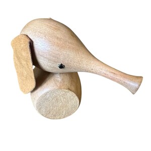 May include: A wooden elephant figurine with a light brown finish. The elephant has a long trunk, large ears, and a small black eye. The figurine is made of wood and has a smooth finish. The elephant is a decorative item.