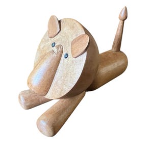 May include: Wooden lion figurine with a light brown finish. The lion has a rounded head, ears, and a long snout. The eyes are small and dark. The legs are cylindrical, and the tail is upright. A decorative wooden toy.